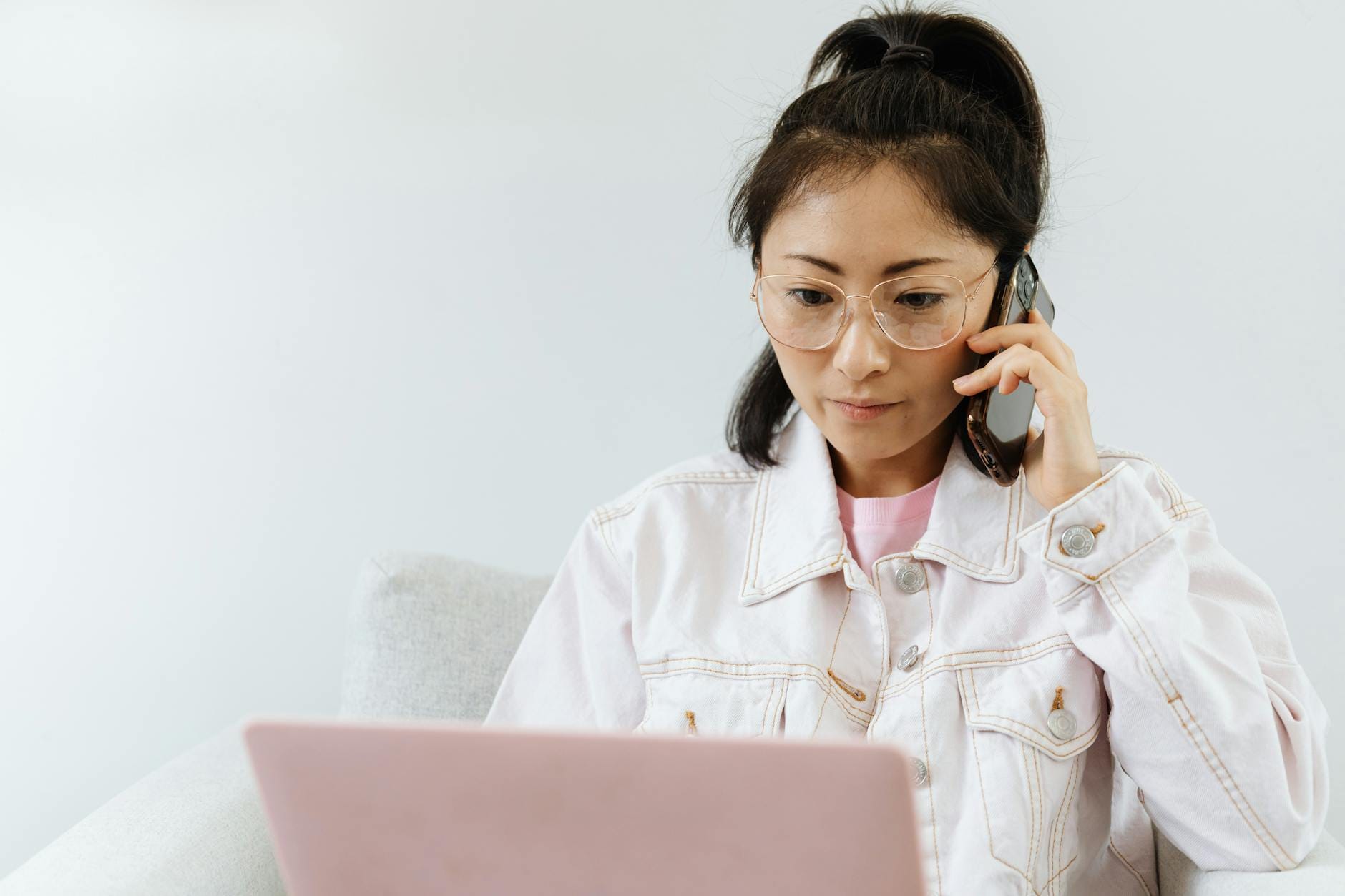 Woman multitasking with phone and laptop in a serene office setting.